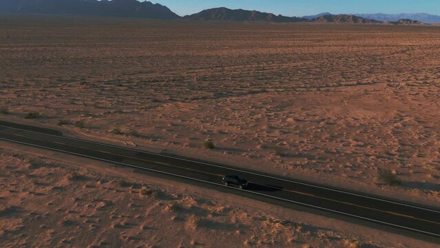 Modern black car driving in the desert on a street from California to Arizona. Scenic sunset landscape.
