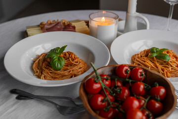 Savory bolognese pasta with basil, prosciutto, cheese, and nuts. A table set with сherry tomatoes, candles, and wine glasses completes a rustic table.