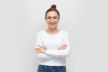 Young woman standing with arms crossed against white background - obrazy, fototapety, plakaty