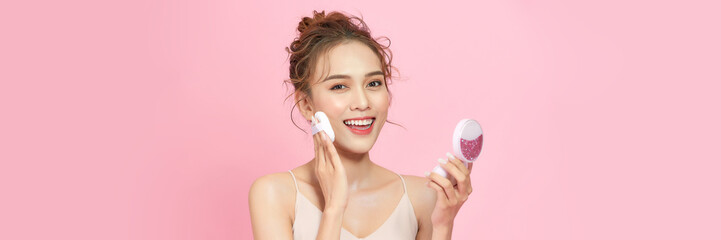 Closeup of beautiful female with cushion puff and mirror applying makeup powder foundation