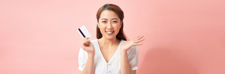 Panoramic orientation of cheerful asian woman holding credit card isolated on pink