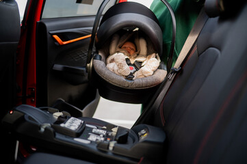 A Caucasian woman puts a child seat with a newborn baby in the car. Quick fastener. 