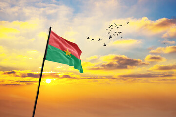 Waving flag of Burkina Faso against the background of a sunset or sunrise. Burkina Faso flag for...