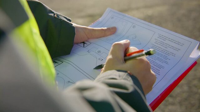 Engineer reading and analyzing schematics on the clipboard while holding a pen, handheld closeup