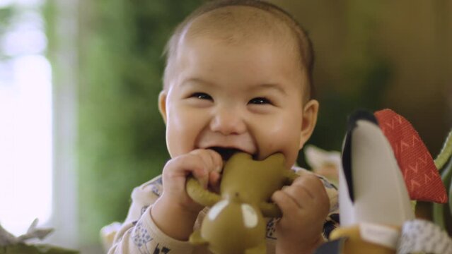 Adorable cute Asian baby smiling and laughing whilst teething and chewing too. Slow motion