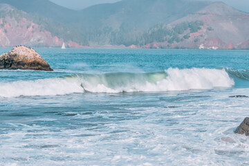Wave splashes close-up. Crystal clear sea water hitting rock formations in the ocean in San Francisco Bay, blue water, pastel colors.