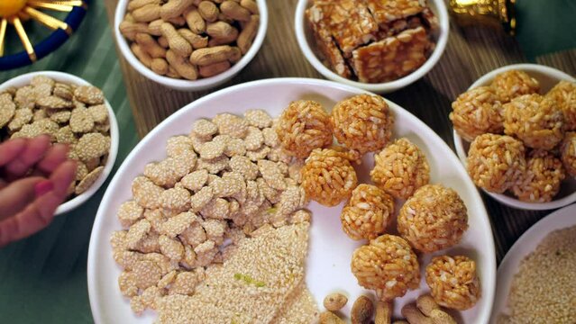 Beautifully served Lohri items consumed on the Lohri festival during wintertime. Closeup shot of Indian woman pouring rewri in a plate surrounded by popcorns  murmure laddoo  peanuts chikki  bhujia...