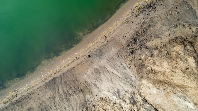 This aerial photograph captures the stark contrast between the lush green hues of a shoreline and the adjacent barren land. The clear demarcation line where the vegetation meets the dry, eroded soil