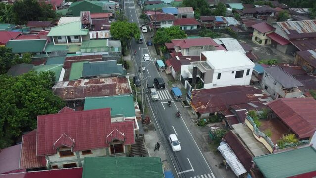 Drone shot of small Philippine road with cars passing by, surrounded by houses, trees, and powerlines.