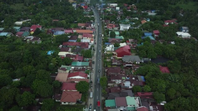Drone shot of Provincial Philippine Highway Road, with cars passing by, surrounded by trees and houses