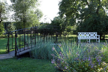 white garden bench for relaxing in the park and a cast-iron bridge over a dry stream