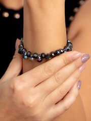 A black bracelet with precious stones is on a girl’s hand