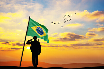 Silhouette of a soldier with the Brazil flag stands against the background of a sunset or sunrise....