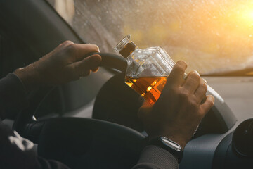 The driver is sitting behind the wheel and holding a bottle of alcoholic drink. Breaking the law and drinking alcohol while driving - obrazy, fototapety, plakaty