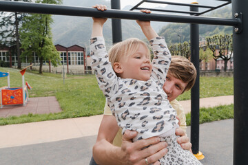 Obraz premium Father supports baby daughter as she hangs from climbing frames