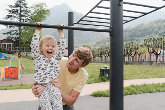 Father supports baby daughter as she hangs from climbing frames