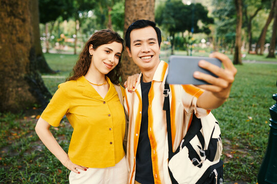 Happy young couple taking selfie on smartphone when walking in park