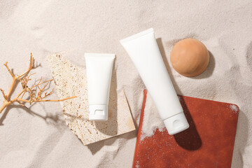 Amidst the white sand background, a wooden branch, wooden ball, unlabeled cosmetic tubes and a...