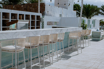 White Exterior of an empty cafe bar counter with mesh bar stools and palm trees in the background on a sunny day. No people
