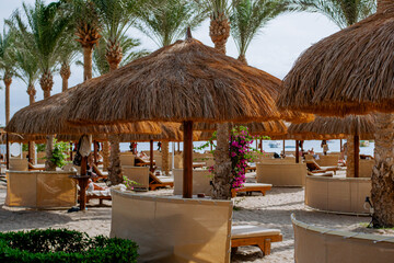 Large straw umbrellas on the beach between palm trees
