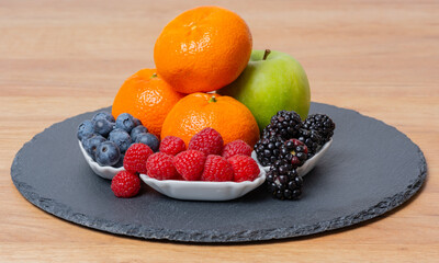 Himbeeren, Brombeeren, Heidelbeeren, Mandarine und Apfel auf einer Schiefertafel