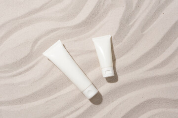 Close-up of two unlabeled cosmetic tubes placed on a sandy background with wave patterns. Mockup...