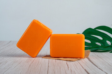 Orange soap on wooden table and and tropical monstera leaves background