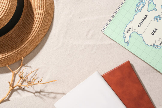 A straw hat, a dry branch, two notebooks and a world map are displayed on the white sand background. Empty space for product display.