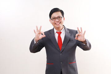 Excited satisfied asian businessman standing while showing okay hand gesture. Isolated on white