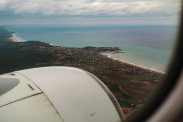 Fototapeta na wymiar view of land from the plane window, sea, town, aircraft engine, cloudy sky, landing position