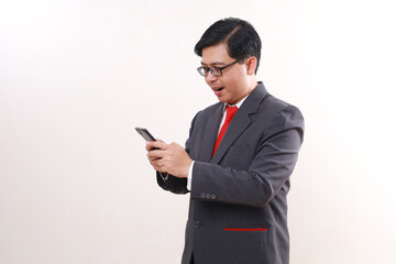 Surprised asian businessman standing while holding a cell phone. Isolated on white