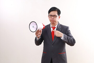 Confused asian business man standing while pointing megaphone on his other hand. Isolated on white