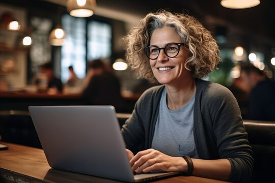 Portrait of smiling mature woman in eyeglasses using laptop in cafe