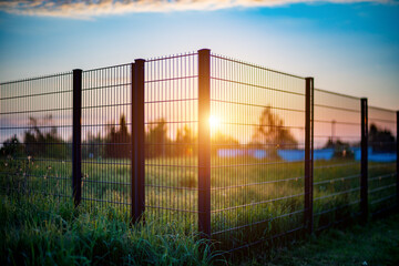  Sunset casts golden light over fence, field, and distant landscape.
