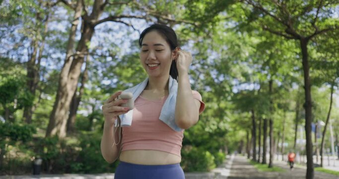 An asian woman preparing for a jog as she utilizes Bluetooth headphones, emphasizing her intention to engage in a running activity while enjoying the convenience of wireless audio technology.