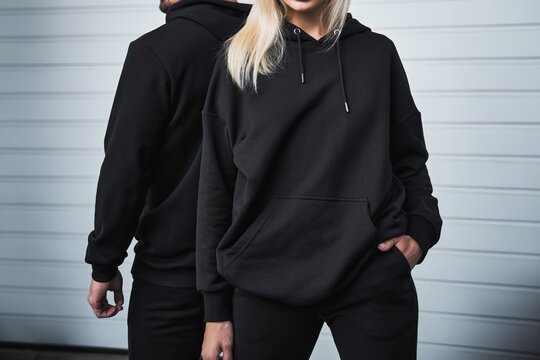 A trendy couple poses outdoors in black hoodies for a mock-up design. A fashion template for print and branding. A casual and elegant street wear style with no face and no logo visible.
