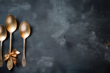 Fotobehang Three gold spoons with a bow on a black background. Ideal for kitchenware or gift-related projects © Fotograf