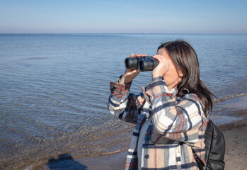 Woman looking through binoculars with the Baltic Sea in the background.