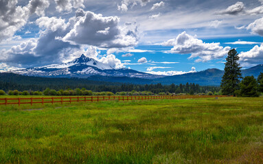 Mount Washington in Oregon with a vibrant green field and wooden fence under a dramatic cloudy sky....