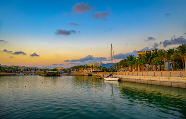 Sunset at Hawana Salalah marina with moored yachts, resorts and palm trees in Oman