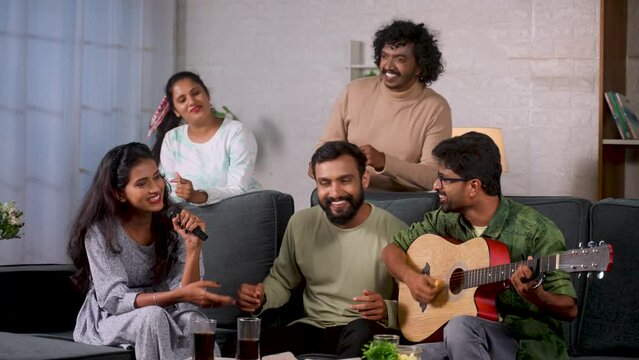 group of happy friends enjoying by playing guitar and singing during home gathering - concept of leisure activities, friendship and recreation
