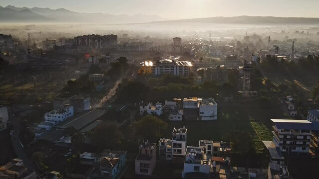 An aerial shot captures a dazzling sunrise over Dehradun city, India. The foggy weather adds to the serene atmosphere, and rows of residential houses are visible from above.