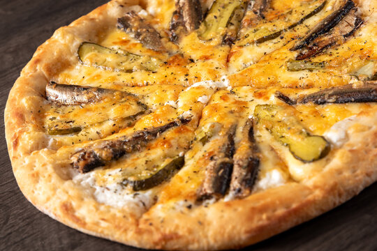 delicious pizza with sprats fish and pickled cucumber on wooden background