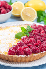 Homemade lemon tart on plate, garnished with fresh raspberry, icing sugar, mint, vertical