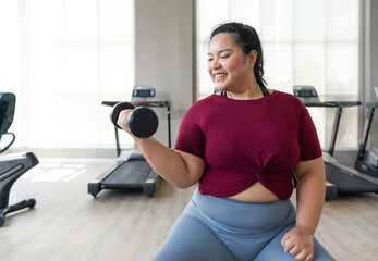 Asian plus-sized woman lifts weights at gym, getting strong and healthy.