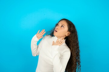 Young beautiful teen girl wearing white turtleneck over blue background keeps palms forward and...
