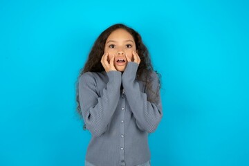 Stupefied Beautiful teen girl wearing blue jacket over blue background expresses excitement and...