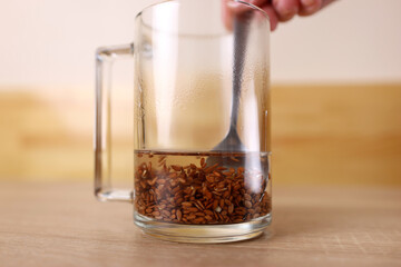 To prepare a therapeutic decoction, flax seeds are shaken in a glass of boiling water. - obrazy, fototapety, plakaty