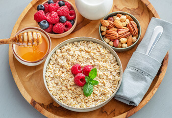 Bowl of porridge or oatmeal with different ingredients on wooden tray. Breakfast serving.