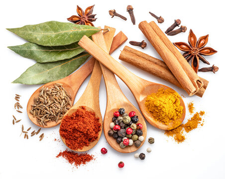 Colorful different seasonings in wooden spoons surrounded with herbs and spices on white background.